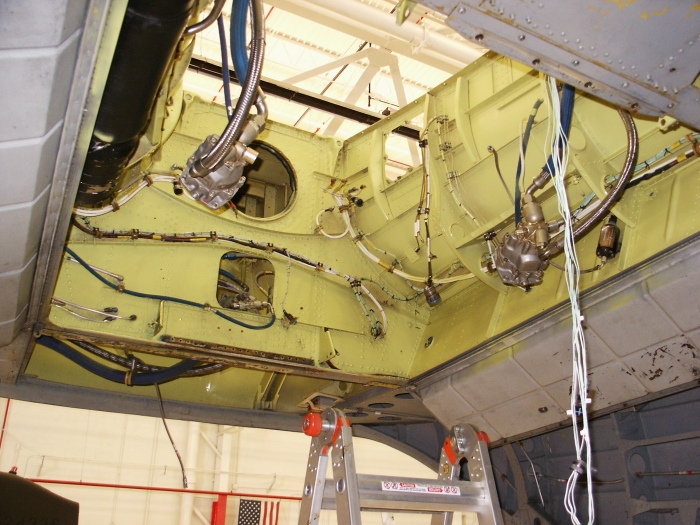 The aft transmission area of CH-47D Chinook helicopter 85-24336 with the aft transmission removed showing the number two flight hydraulic system boost pump (right) and the utility hydraulics system pump (left). The narrow black cylinder to the right of the flight boost pump is the aft transmission pressure transducer.