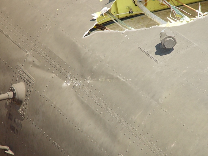 July 2002: A view of the point in which the aft green blade struck the fuselage just above one of the mounts for the HF radio antenna. The fitting to the top right in the image with a cap installed is a vent for the Extended Range Fuel System (ERFS). When that system is installed the cap is removed to allow for the venting of fuel vapors from the internally mounted tanks. There are three of these vents on the CH-47D helicopter.