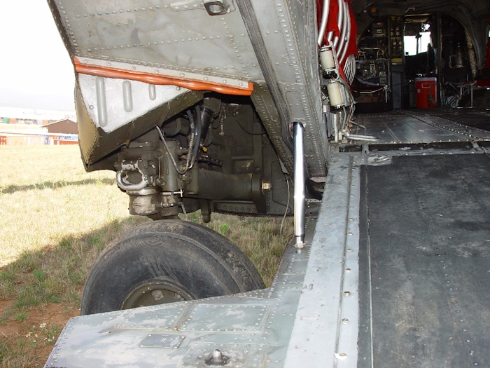 July 2002: A view inside the wheel well for the left aft landing gear. The long vertical shiny, steel colored shaft in the center of the image is one of two ramp actuators that powers up the ramp using hydraulic pressure. The ramp lowers via gravity and is not powered down.