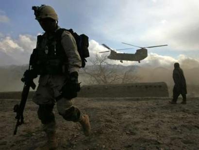 A U.S. soldier (L) and an Afghan man walk away from the dust caused by a Chinook Helicopter in Jegdelic village, about 90 km southwest of Kabul on 24 December 2004. About 200 U.S. service members delivered meals, toys and shoes to villagers of Jegdelic during a day visit to spread goodwill on Christmas Eve.