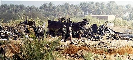 U.S. Army soldiers carry a body bag past the burnt-out wreckage of the downed Chinook helicopter.