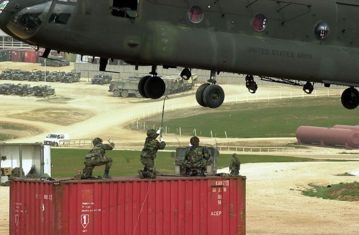 A U.S. Army soldier reaches up to touch a hovering CH-47D Chinook helicopter with a grounding rod as he and his fellow soldiers prepare to sling load a container from Camp Bondsteel, Kosovo.